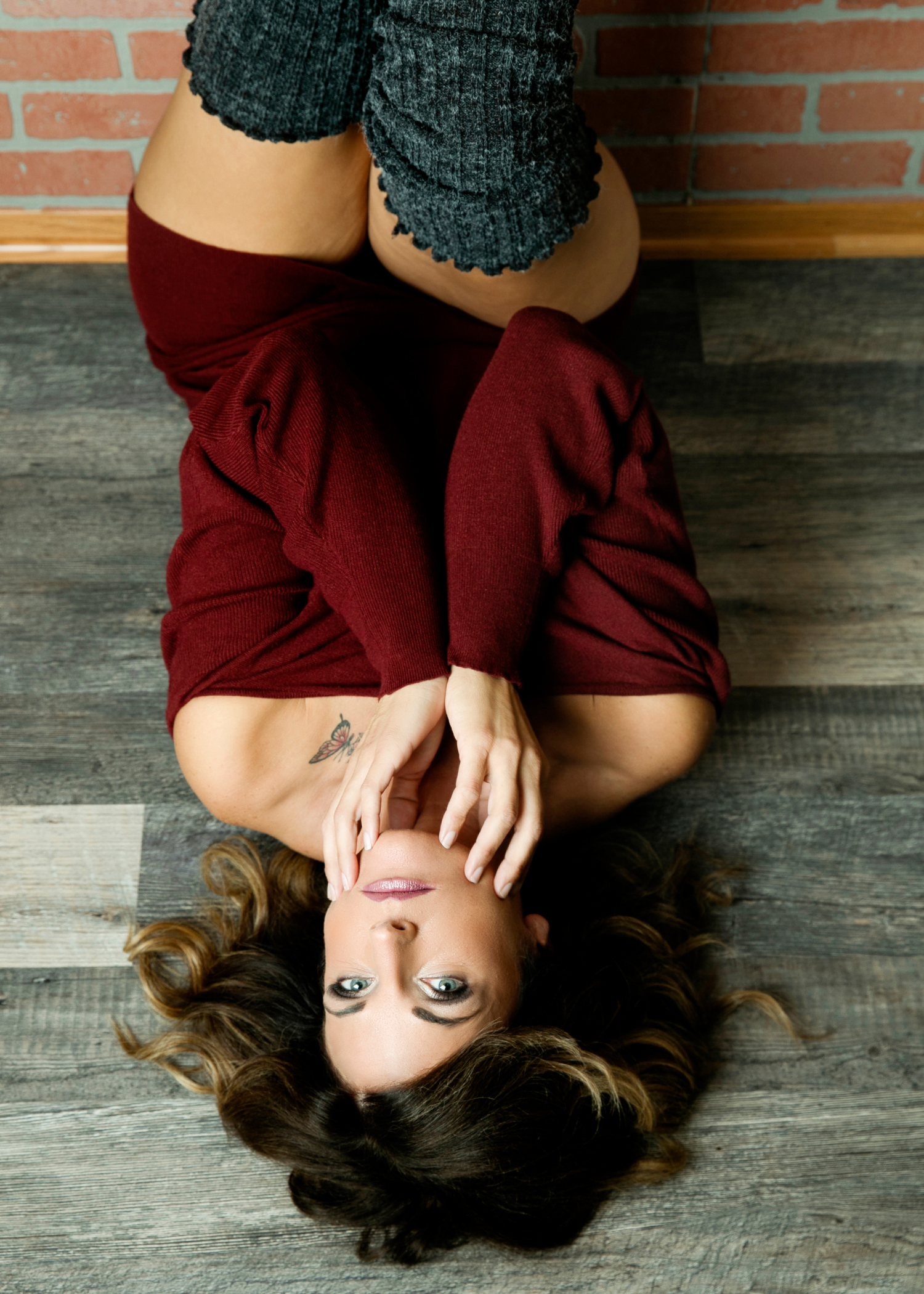 A woman in a maroon sweater lays on the floor with her legs up a brick wall in a studio