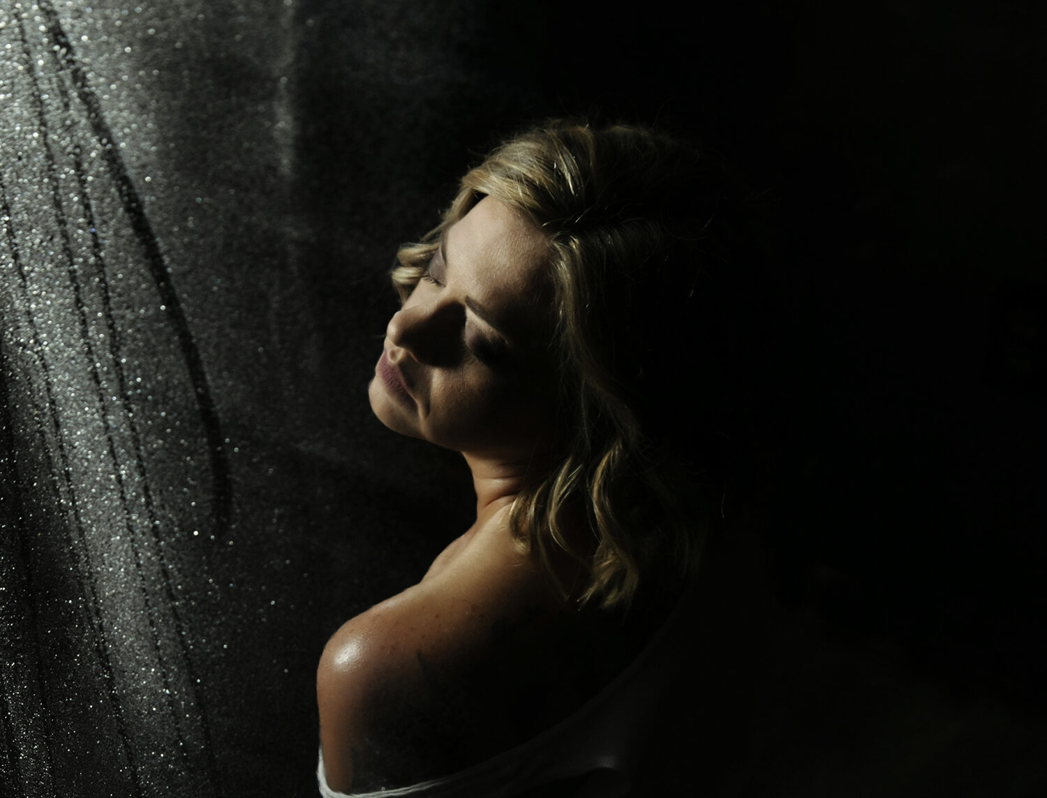 A woman in a white shirt coming off her shoulder sits in a studio behind a wet glass door after using chicago bachelorette party planner